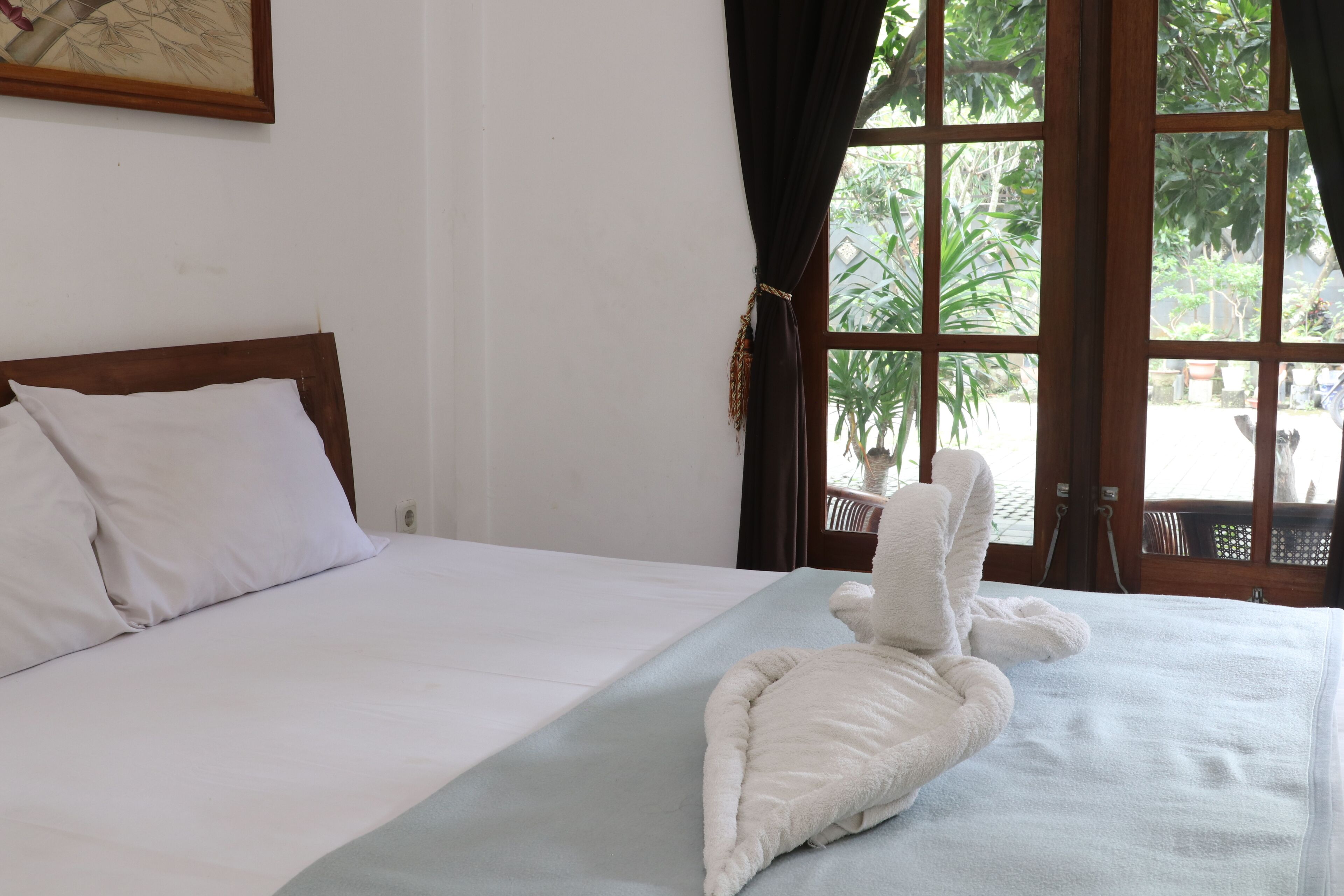 A hotel room with a bed, a window with curtains, and a view of greenery outside.