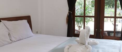 A hotel room with a bed, a window with curtains, and a view of greenery outside.