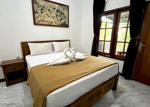 Una cama bien hecha con una manta marrón y almohadas blancas, una mesita de noche pequeña, un cuadro en la pared y una ventana con cortinas.