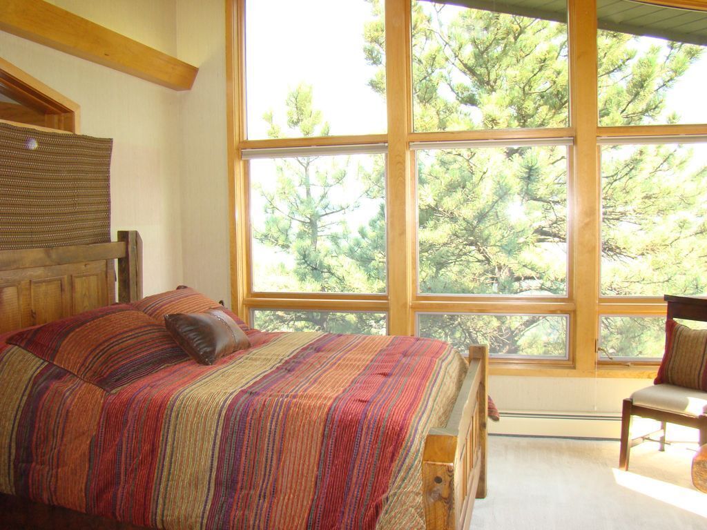 A bedroom with a large window, a bed with a striped bedspread, and a chair.