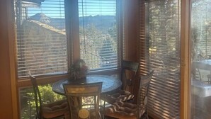 Un coin repas comprenant une table ronde et quatre chaises, de grandes fenêtres équipées de stores et un élément décoratif en métal placé au-dessus des fenêtres.