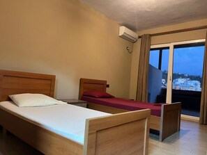 A hotel room with two wooden beds, a window with curtains, and an air conditioning unit.