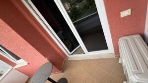 Un balcón con vistas a un área residencial, una pequeña mesa redonda y un armario blanco.