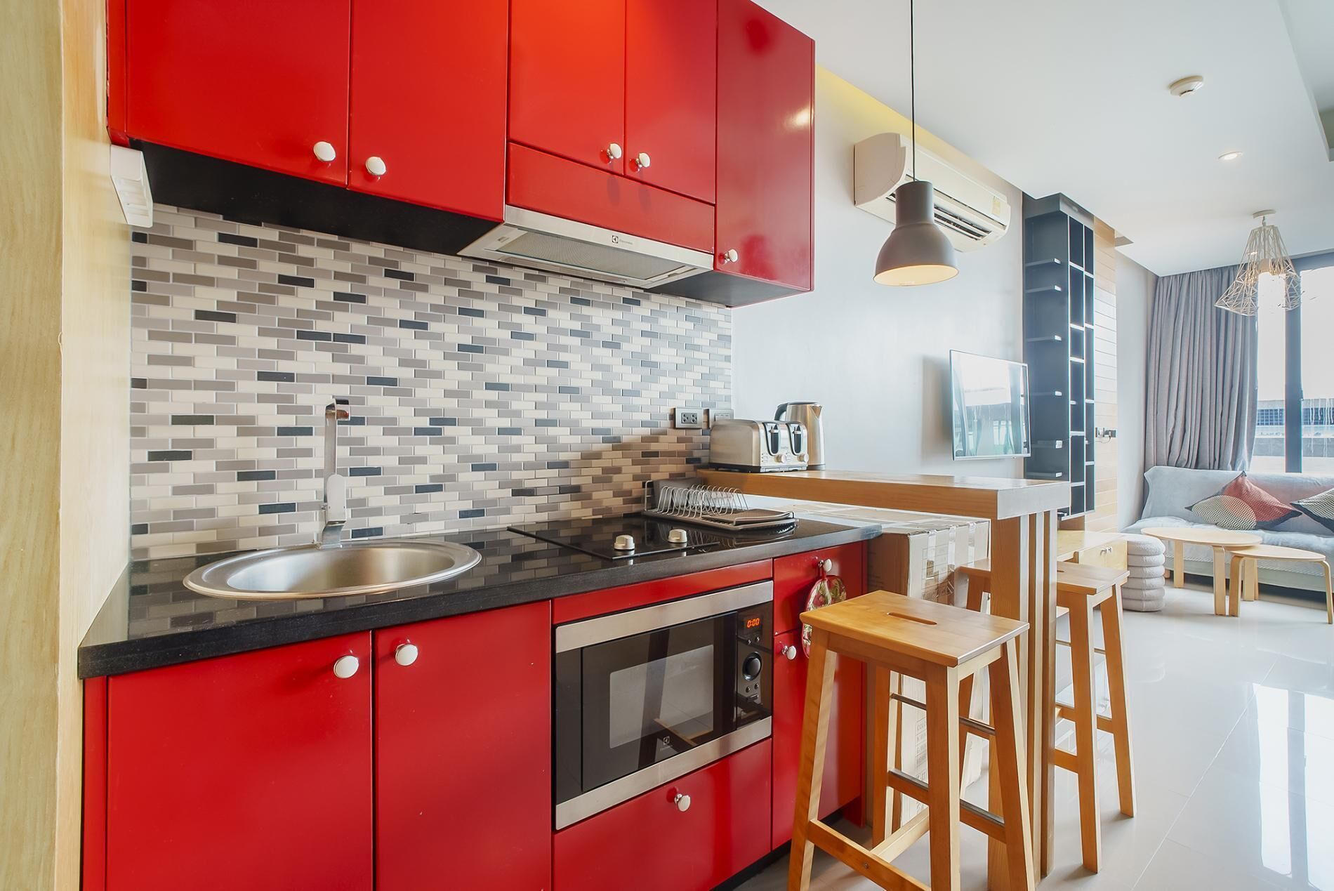 Une cuisine moderne avec des meubles de couleur rouge, un plan de travail noir et un pare-feu en carrelage. On y trouve une cuisinière, un évier et un grille-pain sur le plan de travail.