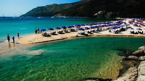 A beach with clear turquoise water, a sandy shore, and numerous blue umbrellas. - 405 Relife , 5 Minutes Walk To Nai Harn Beach (Rawai)