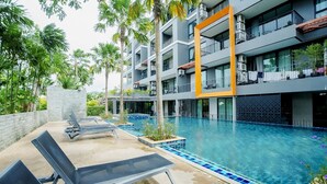 A modern hotel with a swimming pool, lounge chairs, and a multi-story building with balconies. - 405 Relife , 5 Minutes Walk To Nai Harn Beach (Rawai)