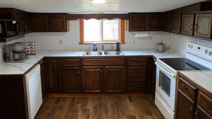 Una cocina con armarios de madera, encimera blanca, un lavabo, una estufa y una ventana sobre el lavabo.