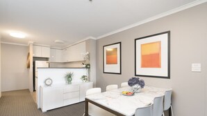 A modern apartment with a kitchen, dining area, and living space. It features a marble dining table, white cabinetry, and artwork on the walls. - Central 2BR apartment, Hotel vibe, Walk everywhere (Braddon)