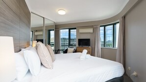 A hotel room with a large bed, a TV, a desk, and a view of the city. - Central 2BR apartment, Hotel vibe, Walk everywhere (Braddon)