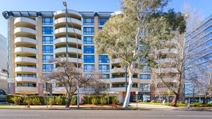 A multi-story hotel with balconies, a landscaped front yard, and a clear sky. - Central 2BR apartment, Hotel vibe, Walk everywhere (Braddon)