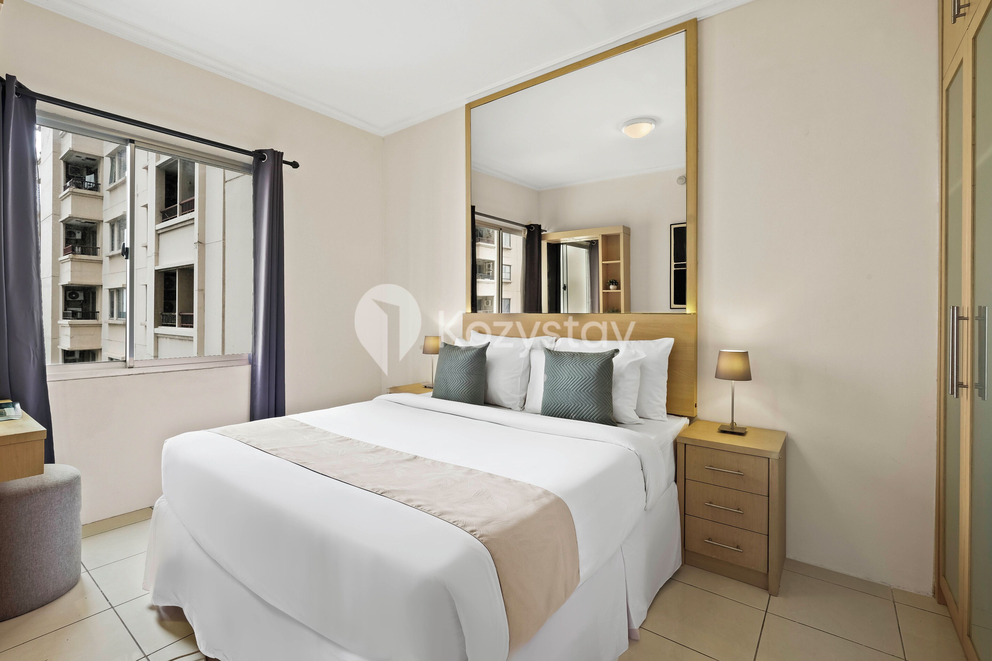 Ein Hotelzimmer mit einem großen Bett, einem Nachttisch mit Lampe, einem Kleiderschrank und einem Fenster mit Vorhängen.