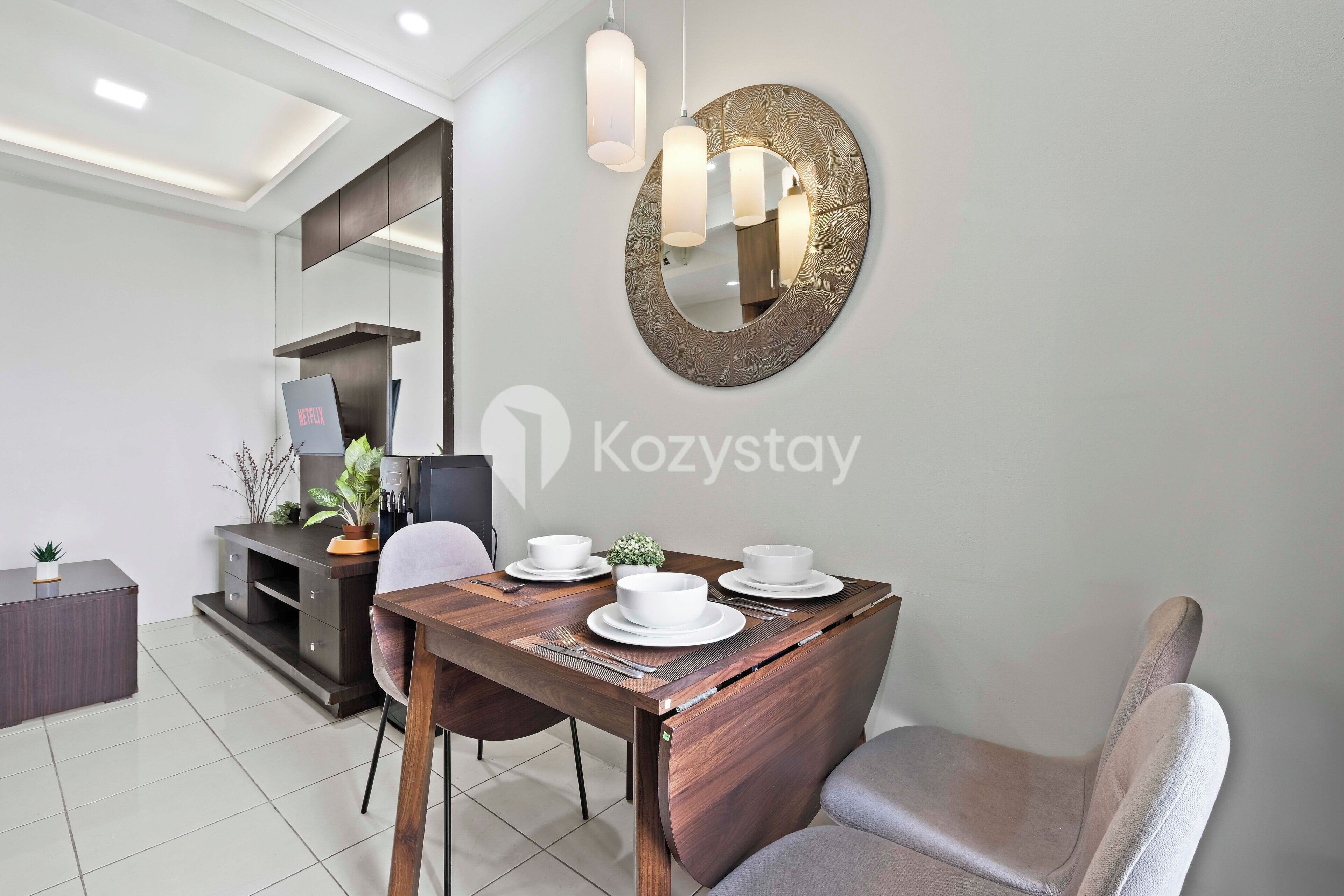 A modern dining area with a wooden table set for two, a large mirror, and pendant lighting.