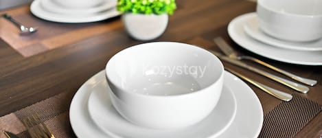 Une table à manger avec des bols et des assiettes blancs, une petite plante en pot et des couverts.