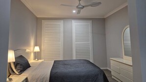 Une chambre à coucher comprenant un lit, des tables de chevet, une lampe, un ventilateur de plafond et une commode.