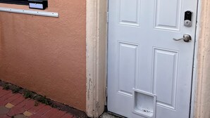 Eine weiße Tür mit einem Zahlenschloss, ein Fenster mit Vorhang und eine strukturierte Wand.
