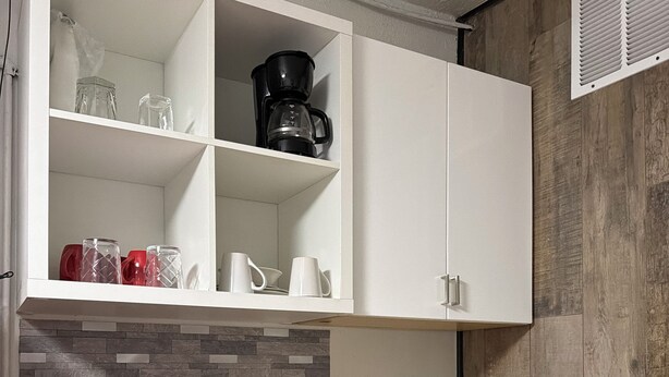 Eine Küche mit weißen Schränken, einer Kaffeemaschine, einem Spülbecken und einer gefliesten Rückwand.