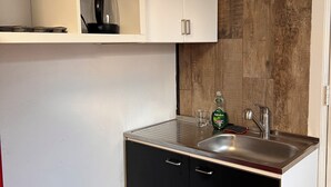 Eine kompakte Küche mit weißen Oberschränken, einem schwarzen Unterschrank, einer Edelstahl-Spüle und einer Holzrückwand.