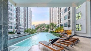 A rooftop pool with lounge chairs, surrounded by high-rise buildings. - The Base Pattaya | Top Location & Utility Include (Bang Lamung, Muang Pattaya)