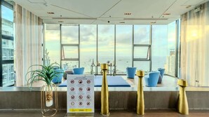 A modern hotel room with large windows, a view of the city, a plant, and a sign with symbols. - The Base Pattaya | Top Location & Utility Include (Bang Lamung, Muang Pattaya)
