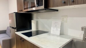 Eine moderne Küche mit Holzschränken, einer eingebauten Mikrowelle, einer Spüle aus Edelstahl und einem grauen Sofa.