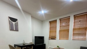 Ein Wohnzimmer mit Holzboden, einem Esstisch mit Stühlen, einem Fernseher und einem Sofa.