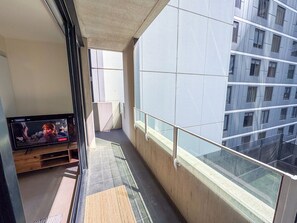 A balcony with a television, a wooden bench, and a view of a building with multiple windows. - Modern CBD Apartment | Pool, Sauna & Laneway Dining (Melbourne)