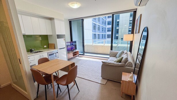 A modern apartment with a dining area, kitchenette, and a balcony with a city view. - Modern CBD Apartment | Pool, Sauna & Laneway Dining (Melbourne)