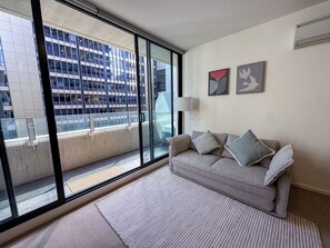 En moderne stue med en stor skydedør, der fører til en balkon, en grå sofa med puder, en gulvlampe og to billeder i rammer på væggen.
