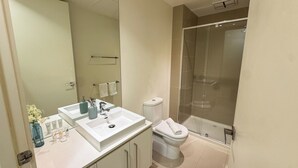 A modern bathroom with a double sink, toilet, and glass shower enclosure. - Modern CBD Apartment | Pool, Sauna & Laneway Dining (Melbourne)