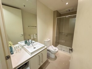 Et moderne badeværelse med dobbelt vask, toilet og glasvægsbad.