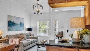Un salon moderne comprenant un canapé, une table basse et des fauteuils, un coin repas avec une table, et une cuisine dotée de meubles en bois et d’un plan de travail.