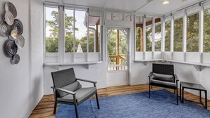 Une véranda avec deux fauteuils, un tapis bleu et une vue sur l’extérieur.