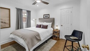 Une chambre à coucher avec un lit, un ventilateur de plafond, une table de chevet avec une lampe, une chaise et une porte.