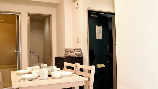 Et spiseområde med et bord dækket til fire personer, en stol og et lille skab med håndklæder.