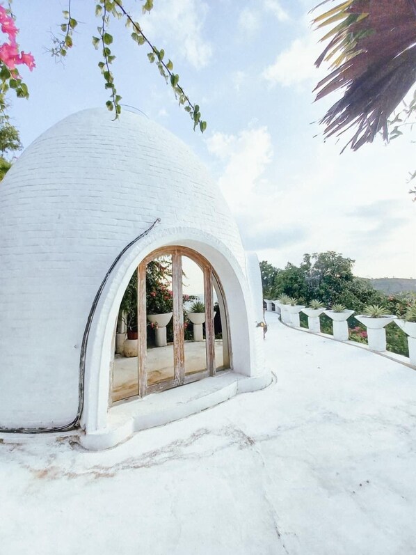 A white dome-shaped structure with a large arched window, surrounded by a white fence and potted plants. - Mentigibay Dome Villa Lombok (Pemenang)
