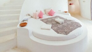 A modern, white-themed bedroom with a circular bed, a small seating area, and a staircase leading to an upper level. - Mentigibay Dome Villa Lombok (Pemenang)