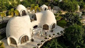 A white, dome-shaped building with multiple arched doorways and windows, surrounded by lush greenery. - Mentigibay Dome Villa Lombok (Pemenang)