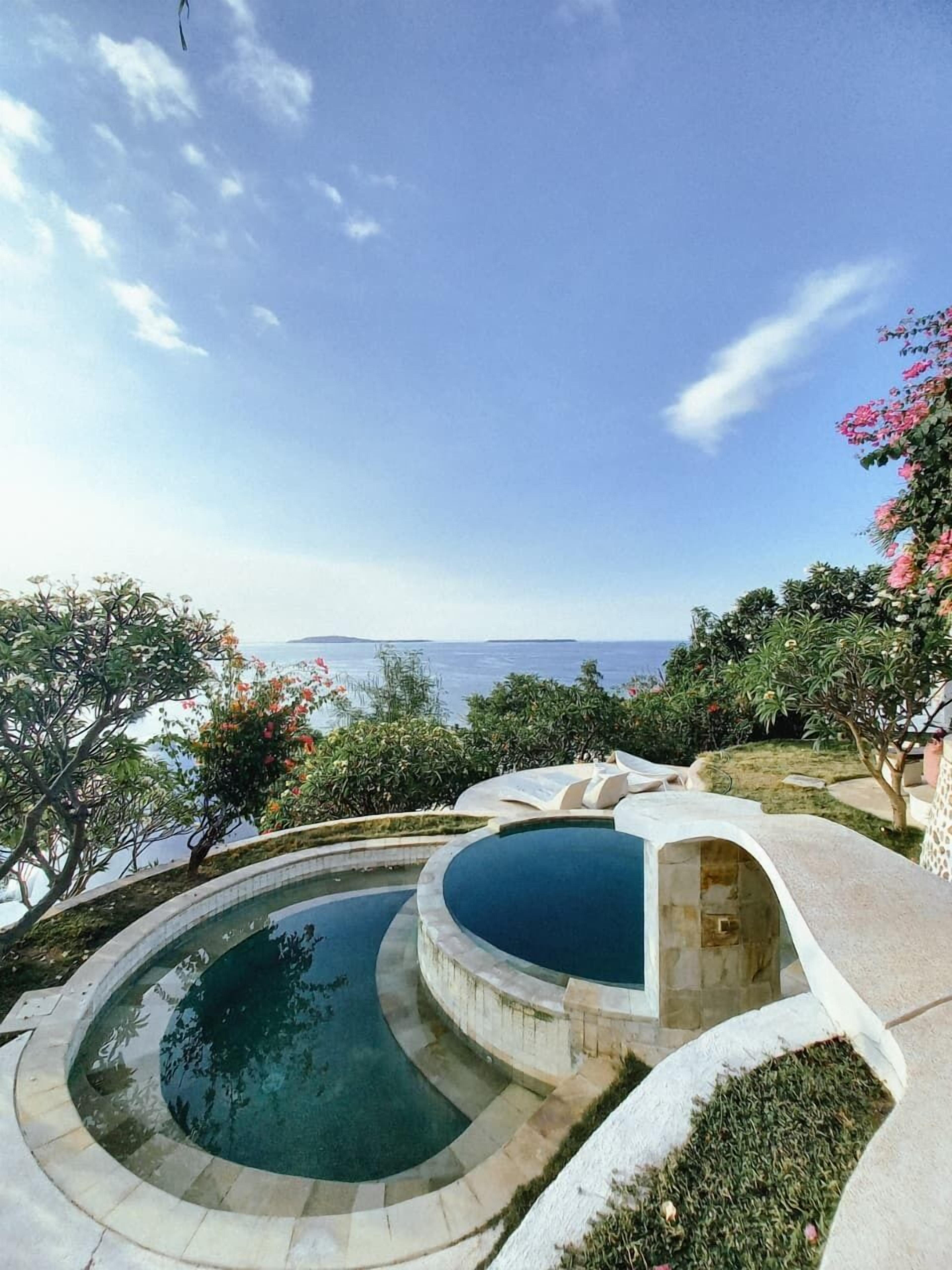 A pool with a circular design, surrounded by a stone deck and lush greenery.