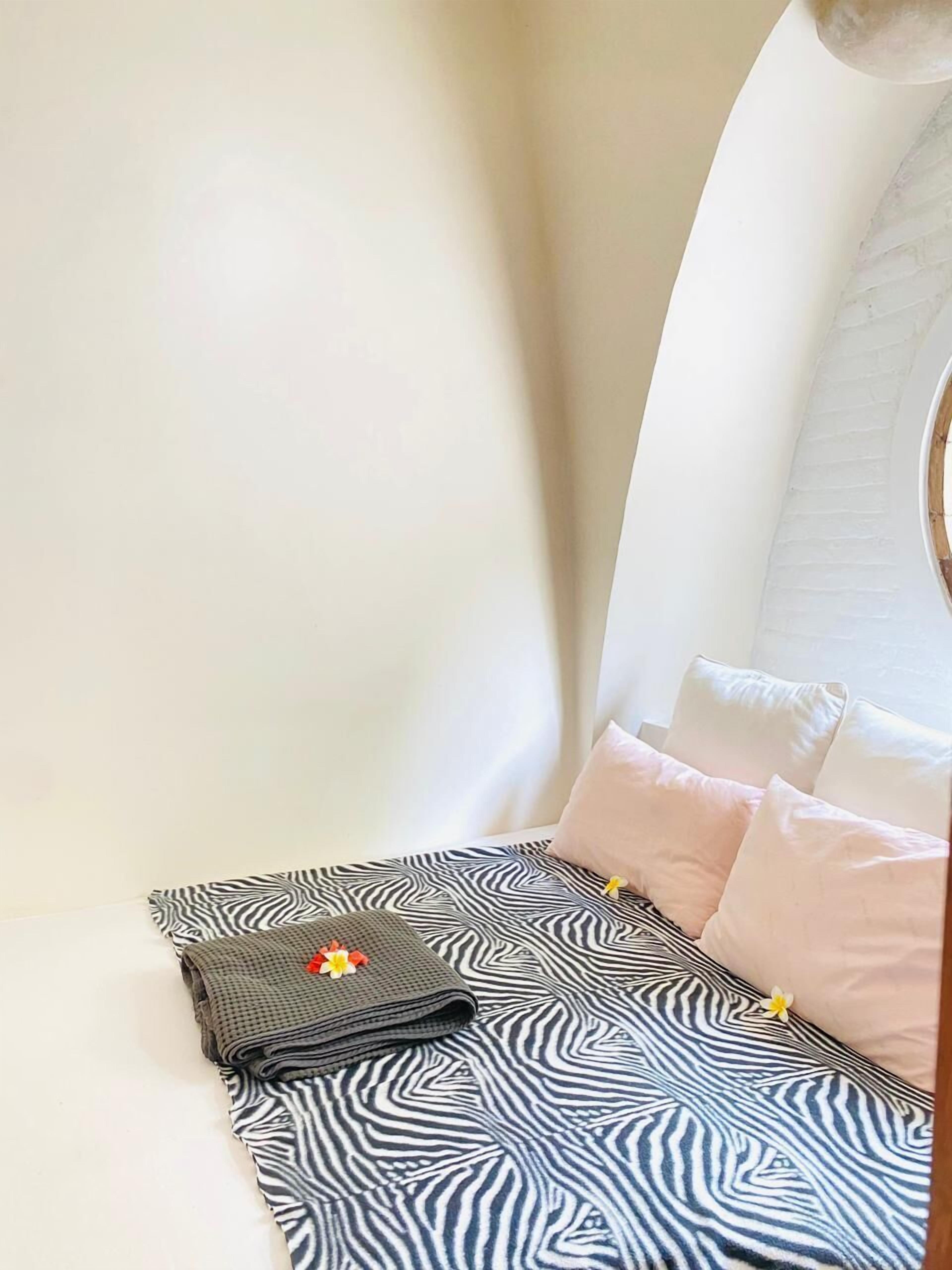 A neatly made bed with a zebra-patterned bedspread, a folded towel with a flower, and a small round mirror on the headboard.
