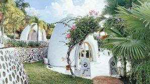 A series of white, dome-shaped structures with arched doorways, surrounded by lush greenery and a clear sky. - Mentigibay Dome Villa Lombok (Pemenang)