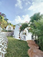 Una serie de estructuras blancas en forma de cúpula con puertas arqueadas, rodeadas de exuberante vegetación y un cielo despejado.