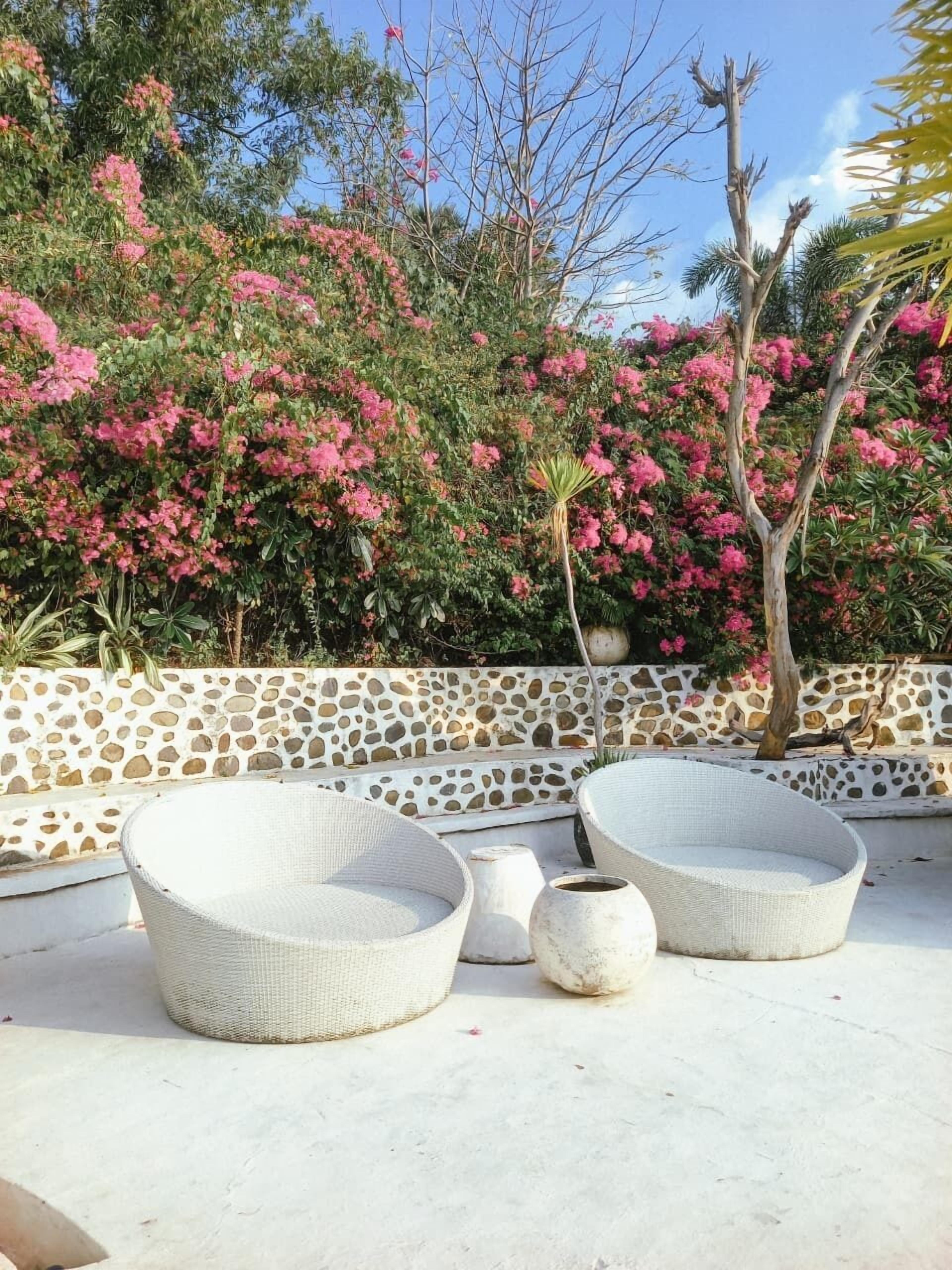 An outdoor seating area with wicker chairs and a stone wall backdrop.