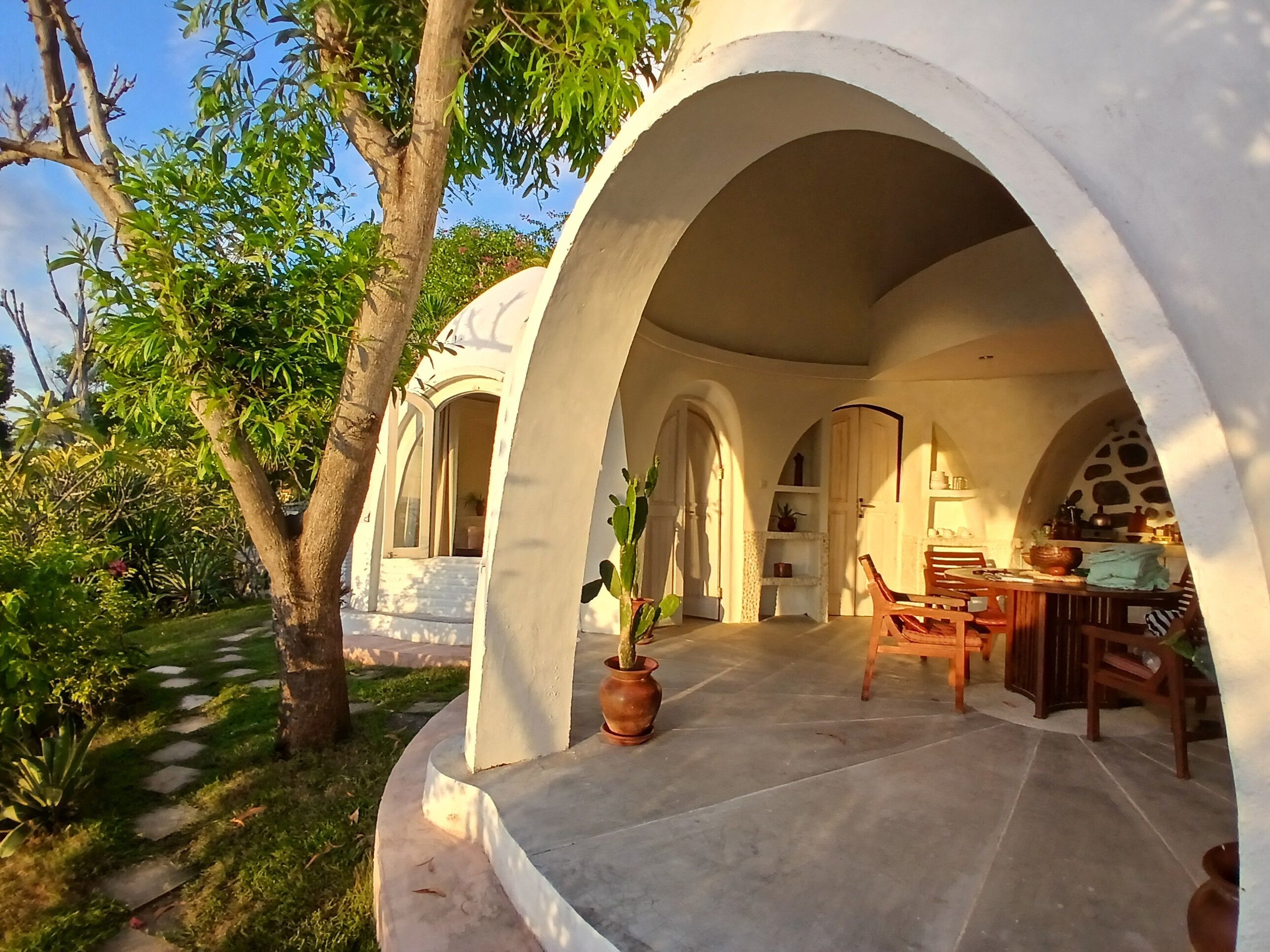 A covered outdoor area with a stone floor, wooden furniture, and potted plants.