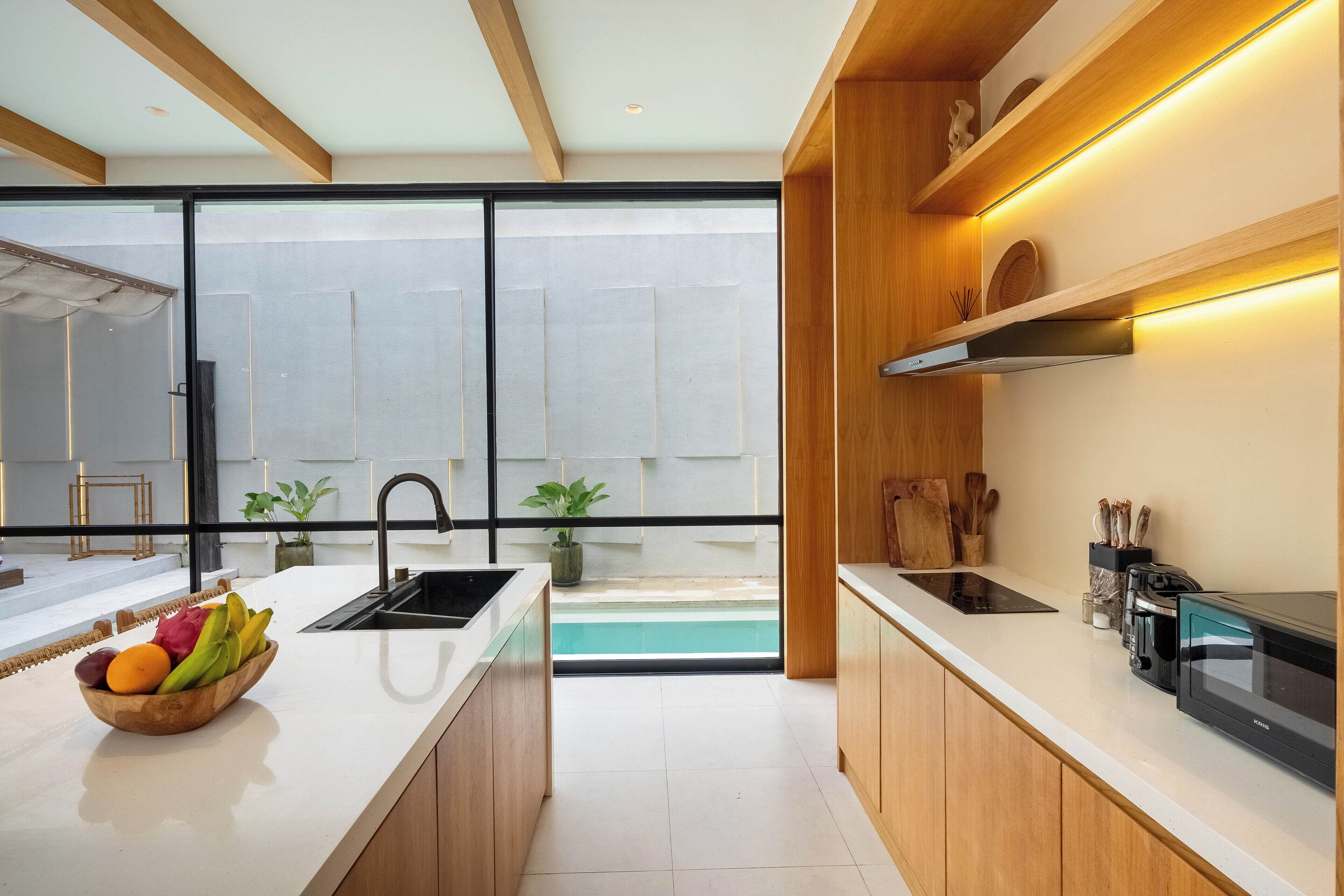 Een moderne keuken met een groot eiland, een inbouwoven en uitzicht op een zwembad door de glazen deuren.