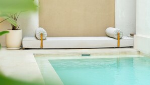 A poolside relaxation area with a white lounge chair and a potted plant. - Villa Thre by Pertama Stay (Canggu)