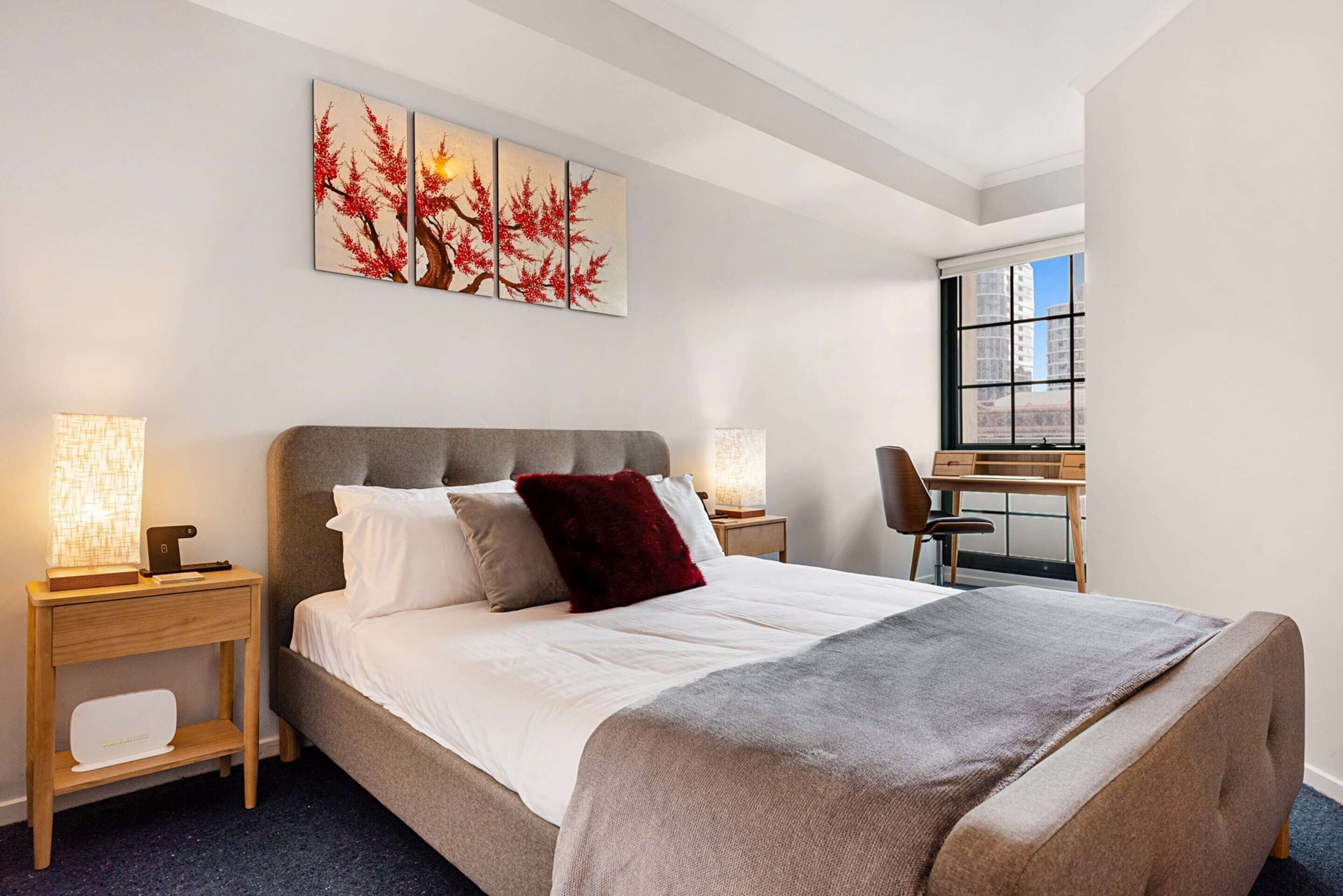 A neatly arranged bedroom with a bed, bedside tables, a desk, and a window.