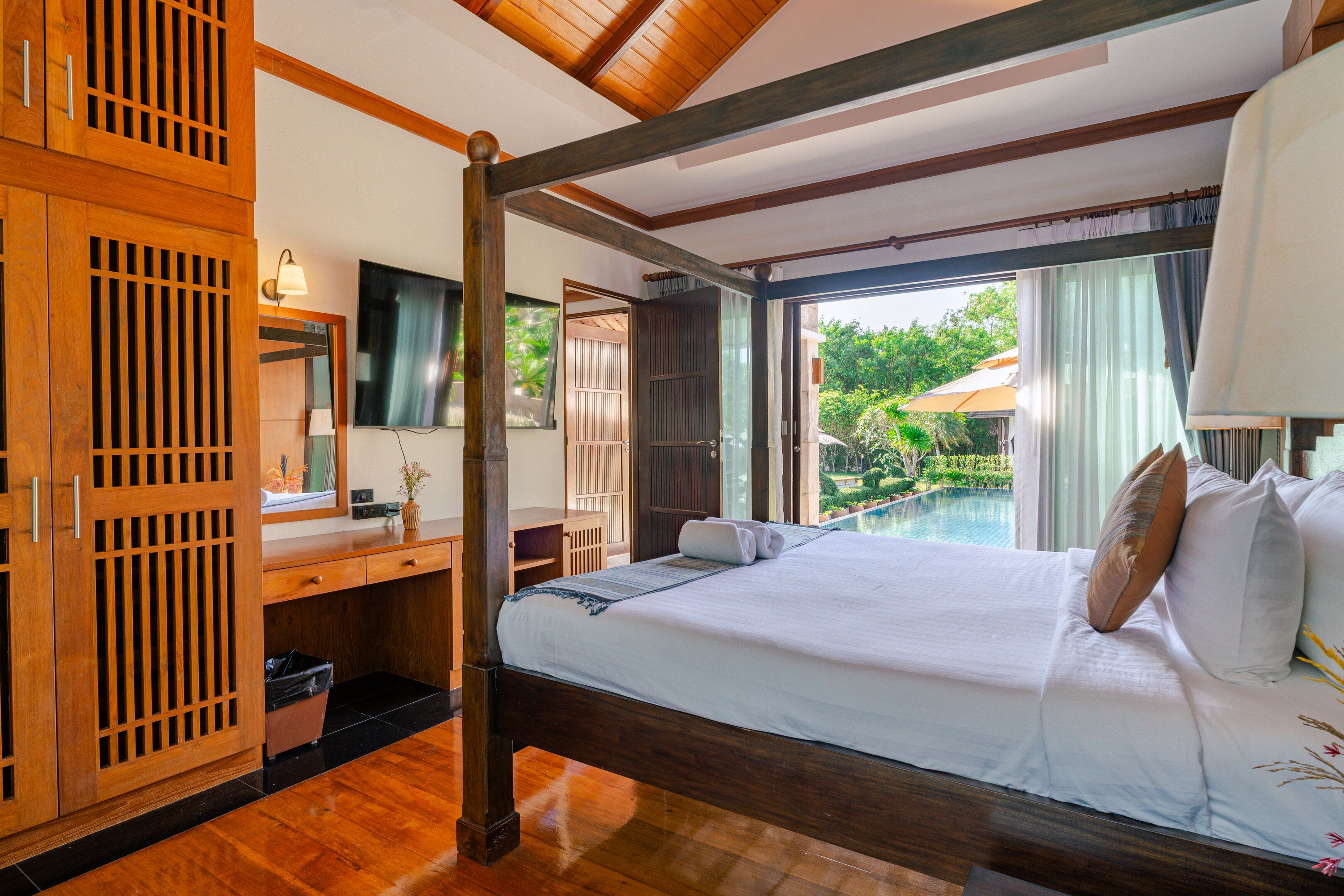 Habitación de hotel con cama, escritorio, televisor y vista a una piscina al aire libre.