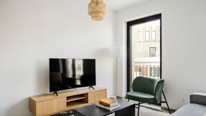 Una sala de estar moderna con un televisor de pantalla plana sobre un soporte de madera, una silla verde, un sofá gris y una mesa de centro negra.