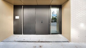 Una entrada moderna de edificio con puertas dobles, una barandilla metálica y suelo de baldosas.