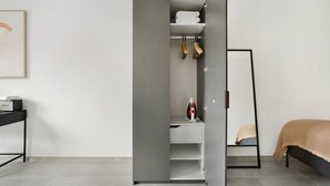 Un dormitorio moderno con un armario gris, una cama con una manta color beige y un soporte de metal negro.